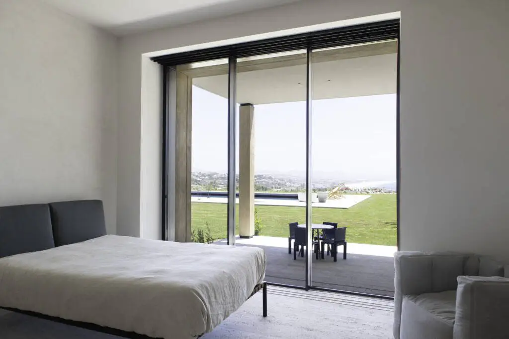 Bedroom slider opening to lawn, pool, and city panorama